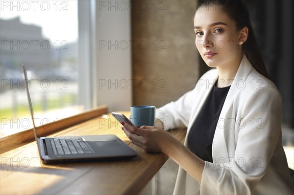 Caucasian woman texting on cell phone and drinking coffee
