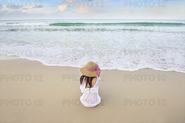 Woman sitting on beach near ocean waves