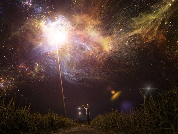 Caucasian man reaching towards light in starry night sky