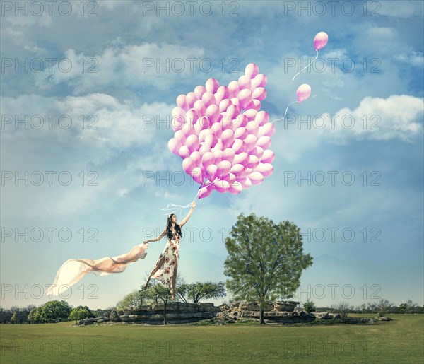 Chinese woman being lifted in field by bouquet of pink balloons