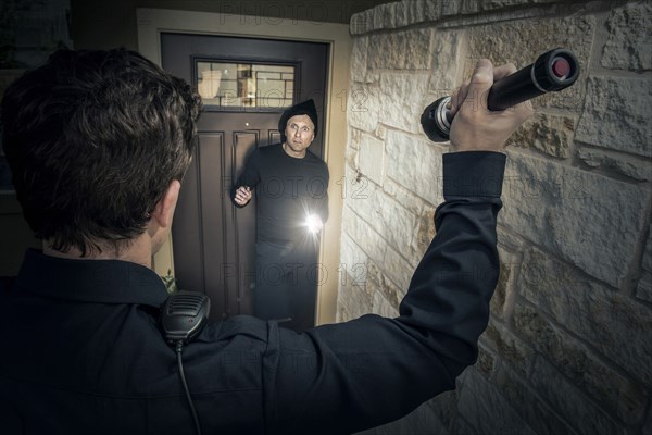 Caucasian police officer shining flashlight on house burglar