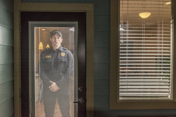 Caucasian security officer standing behind door with blinds