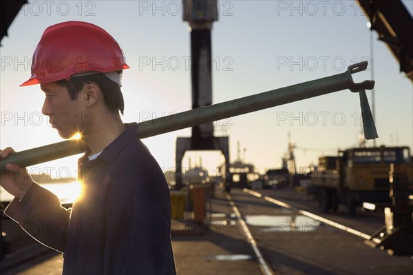 Asian male construction worker carrying pipe