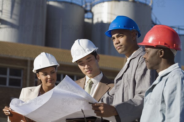 Multi-ethnic businesspeople and construction workers looking at blueprints