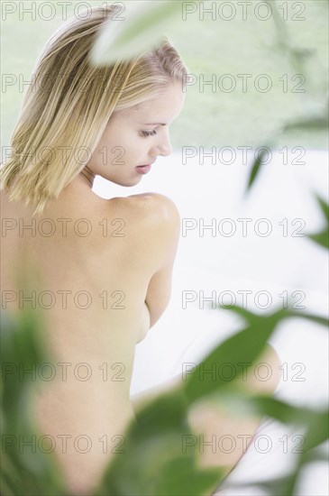 Nude woman sitting behind plant