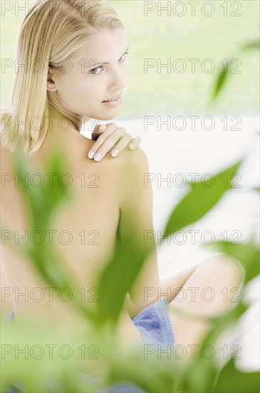 Nude woman sitting behind plant