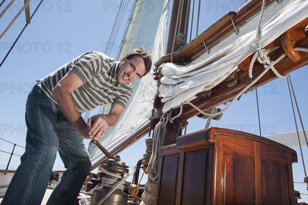 Caucasian man hoisting sail on sailboat