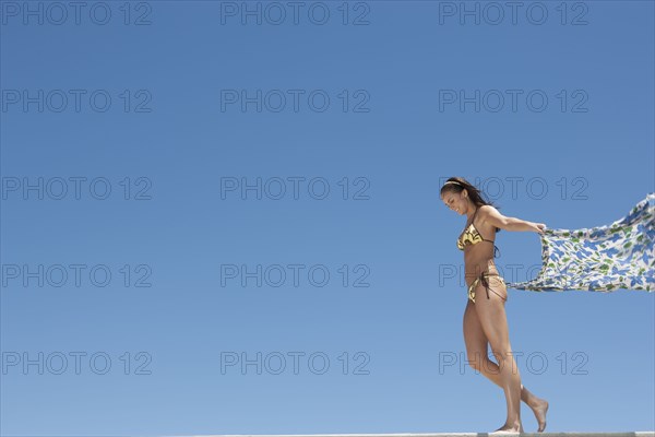 Caucasian woman in bikini holding sarong in wind