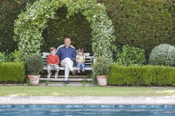 Grandfather sitting with grandchildren on garden bench