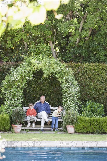 Grandfather sitting with grandchildren on garden bench