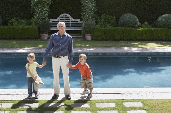 Grandfather and grandchildren standing at poolside