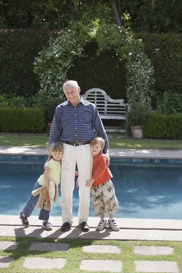 Senior Caucasian man hugging grandchildren by pool