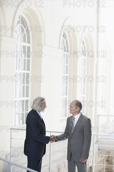 Senior Caucasian businessmen shaking hands on balcony