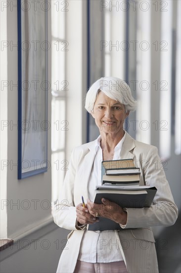 Senior Caucasian businesswoman carrying books in office