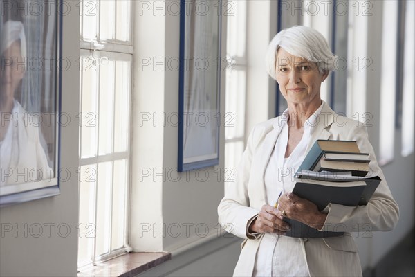 Senior Caucasian businesswoman carrying books in office