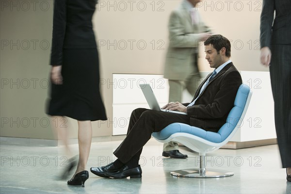 Businessman working on laptop in busy lobby area