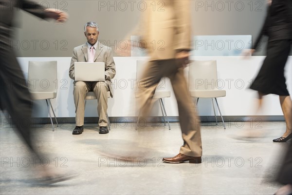 Businessman using laptop in busy lobby area