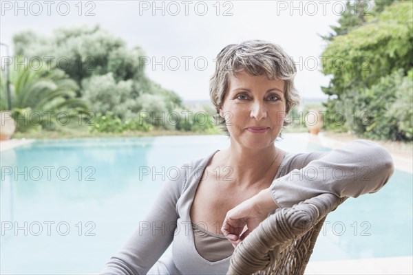 Woman smiling in armchair by swimming pool
