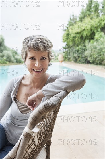 Woman smiling in armchair by swimming pool