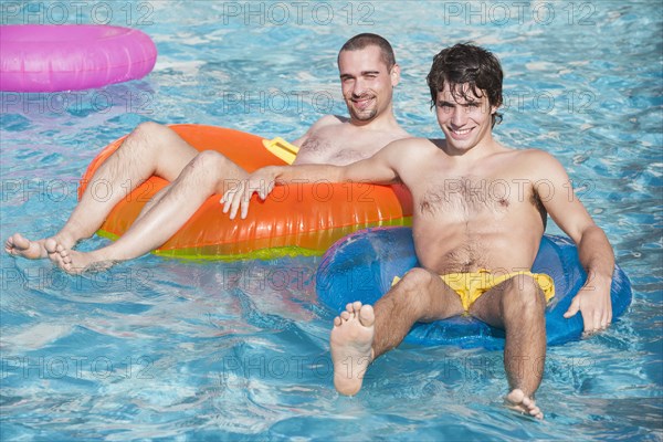 Men floating in inner tubes in swimming pool