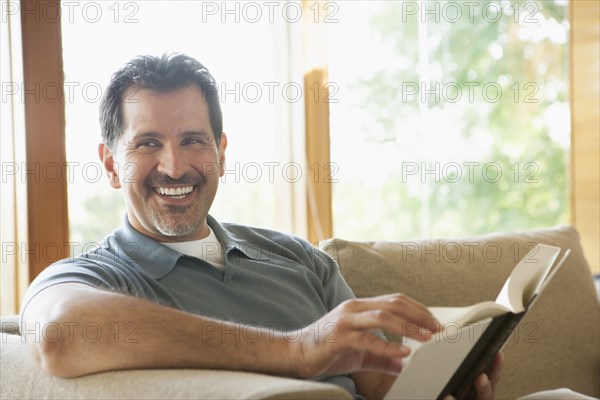 Hispanic man reading on sofa