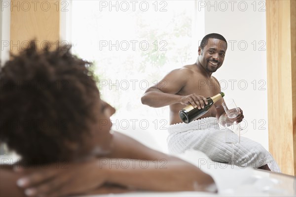 African American couple drinking champagne in bath