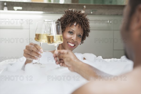 African American couple drinking champagne in bath