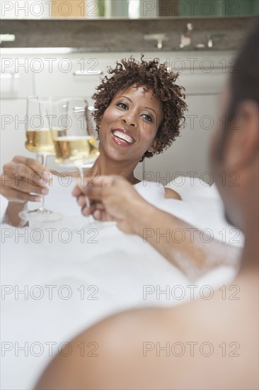 African American couple drinking champagne in bath