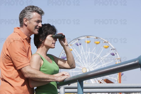 Caucasian couple using binoculars at theme park