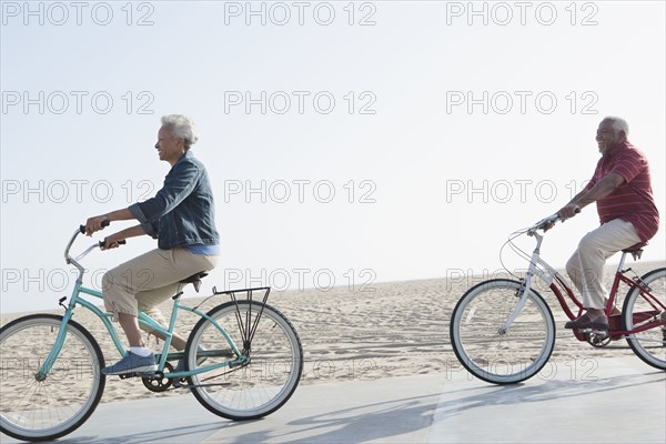 Senior African American couple riding bicycles by beach