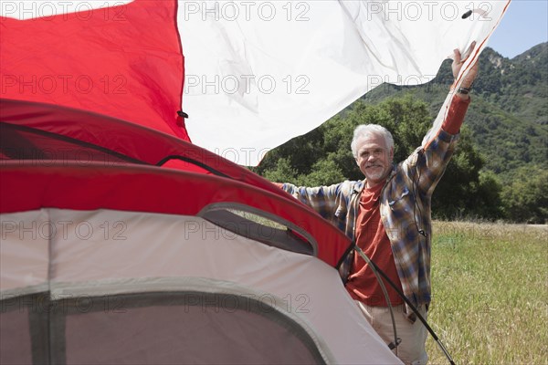 Senior Caucasian man pitching tent in field