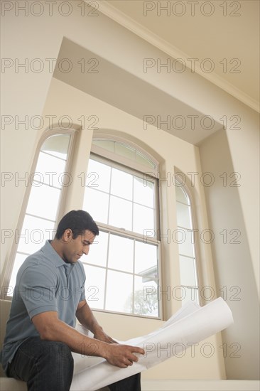 Hispanic man reading blueprints in new home