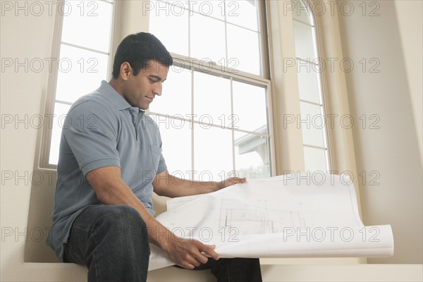 Hispanic man reading blueprints in new home