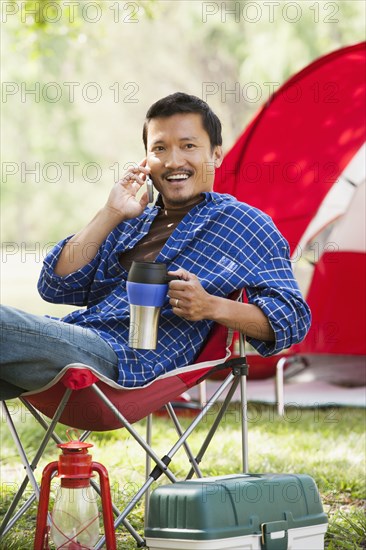 Asian man relaxing in lawn chair at campsite