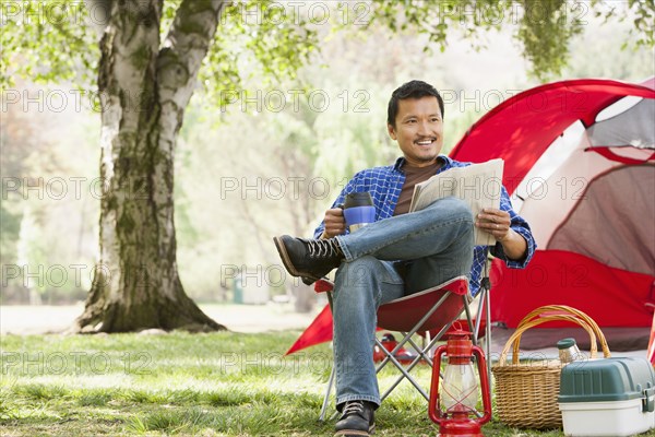 Asian man relaxing in lawn chair at campsite