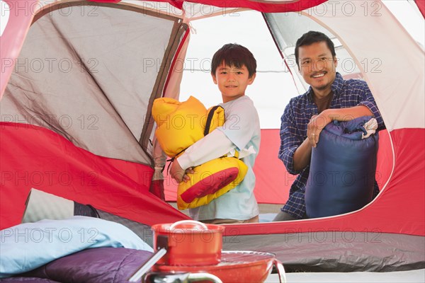 Asian father and son unpacking in tent