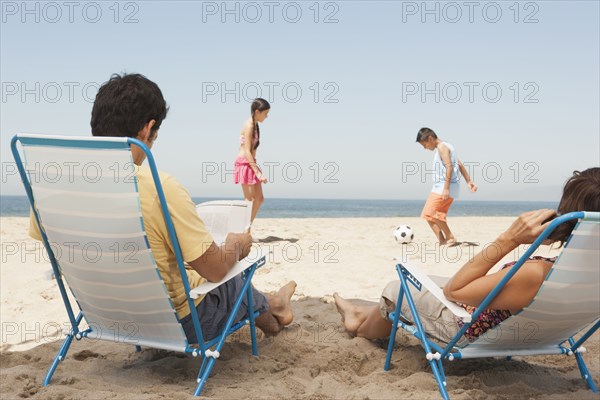 Parents watching children from lawn chairs on beach