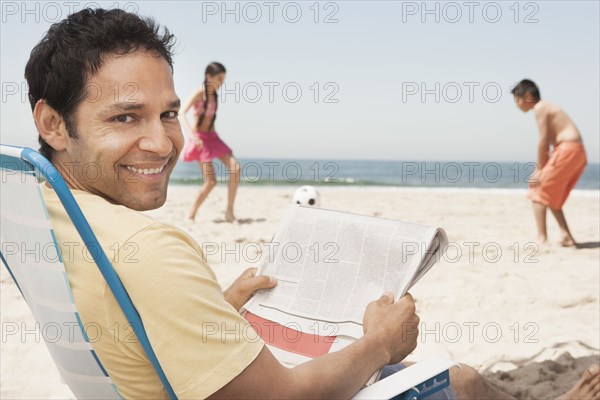 Hispanic father relaxing as children play on beach