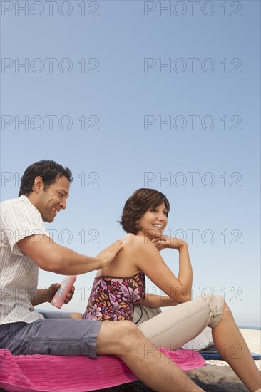 Man rubbing sunscreen on girlfriend's shoulders