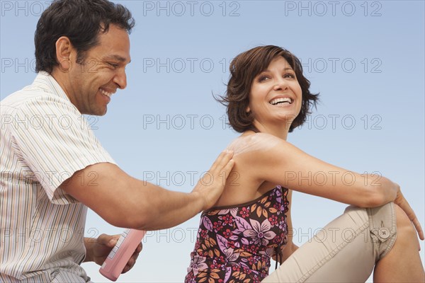 Man rubbing sunscreen on girlfriend's shoulders