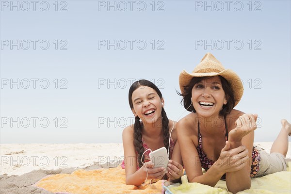 Mother and daughter listening to headphones on beach