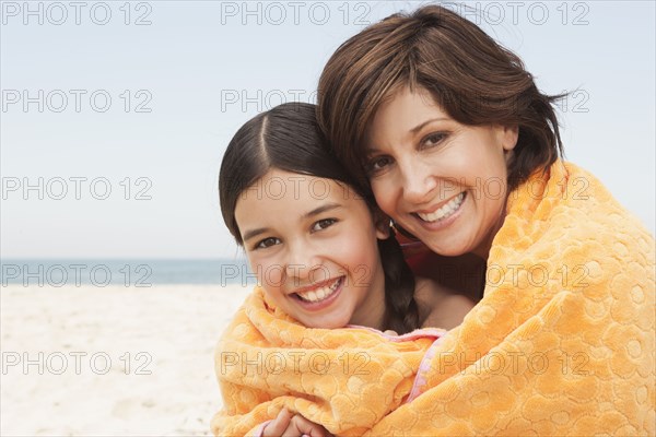 Mother and daughter wrapped in towel on beach
