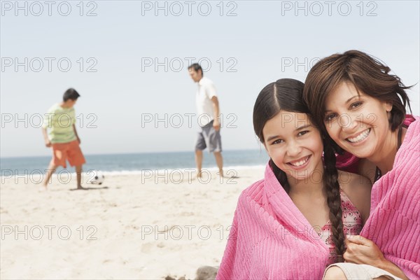 Mother and daughter wrapped in towel on beach