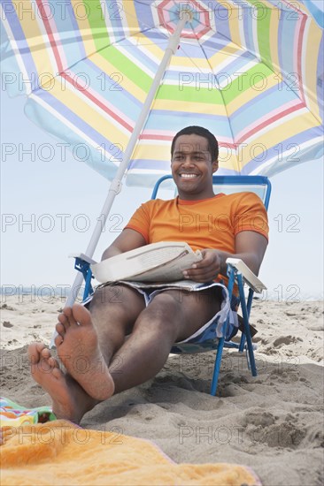 Mixed race man sitting in lawn chair on beach