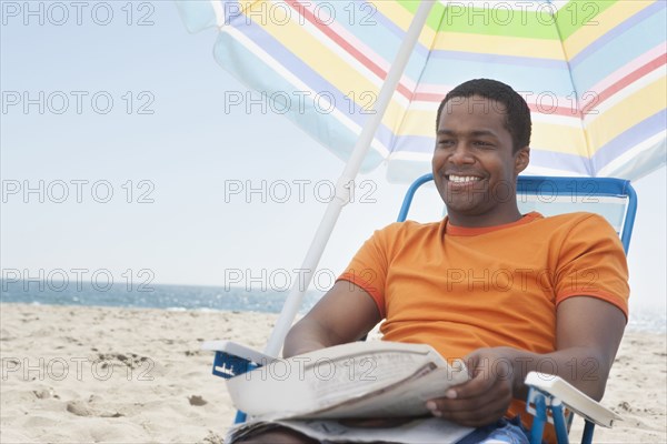 Mixed race man sitting in lawn chair on beach