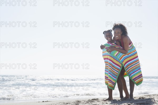 Mother and daughter wrapped in towel on beach