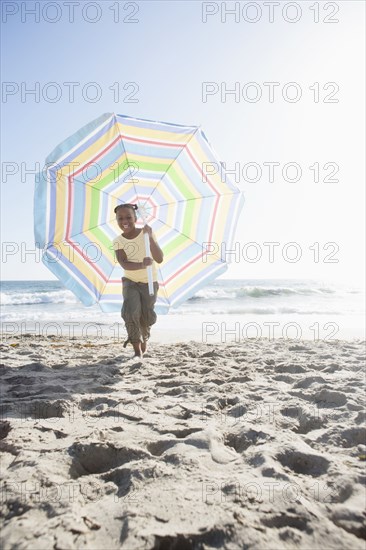 African American girl carrying umbrella on beach