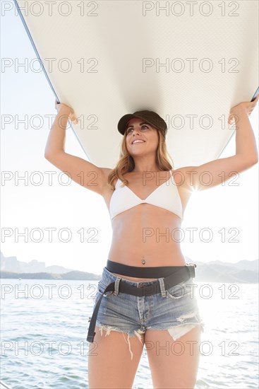 Hispanic woman carrying paddleboard near river