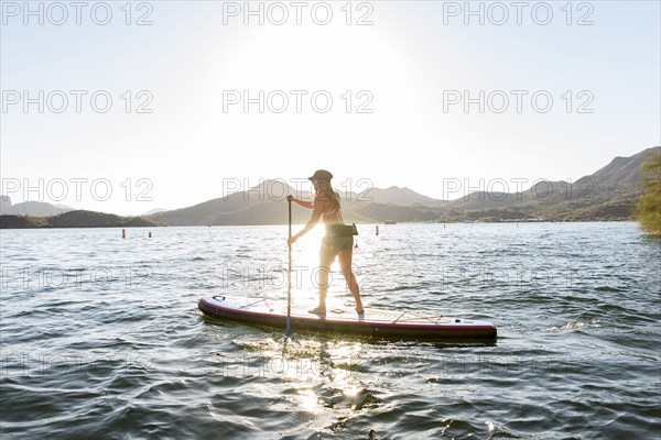 Hispanic woman standing on paddleboard in river