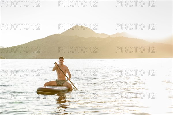 Caucasian man sitting on paddleboard in river